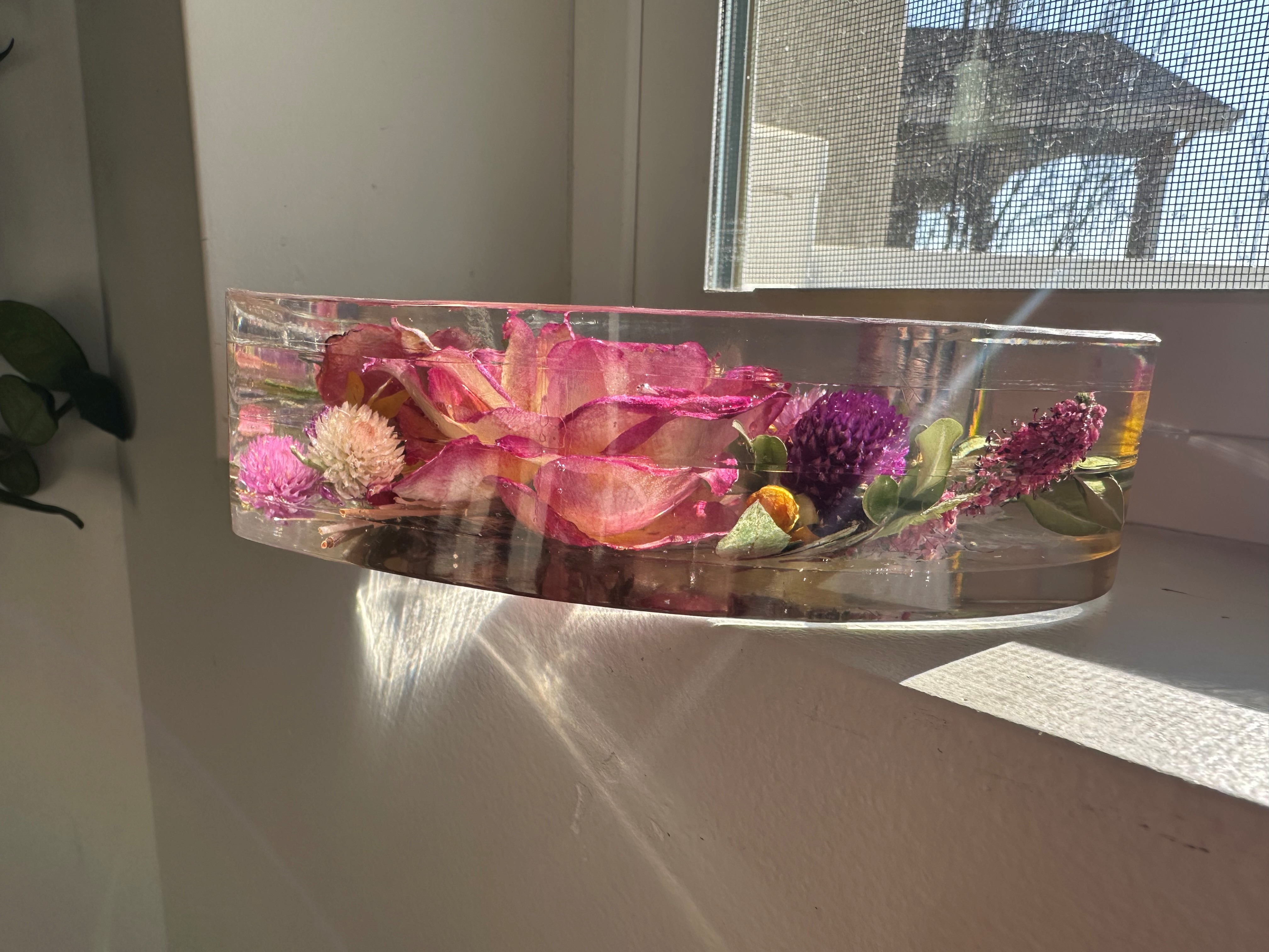 Resin-encased flowers in the shape of a heart as seen from the side, showcasing the depth of the resin pour with layered colors and natural elements