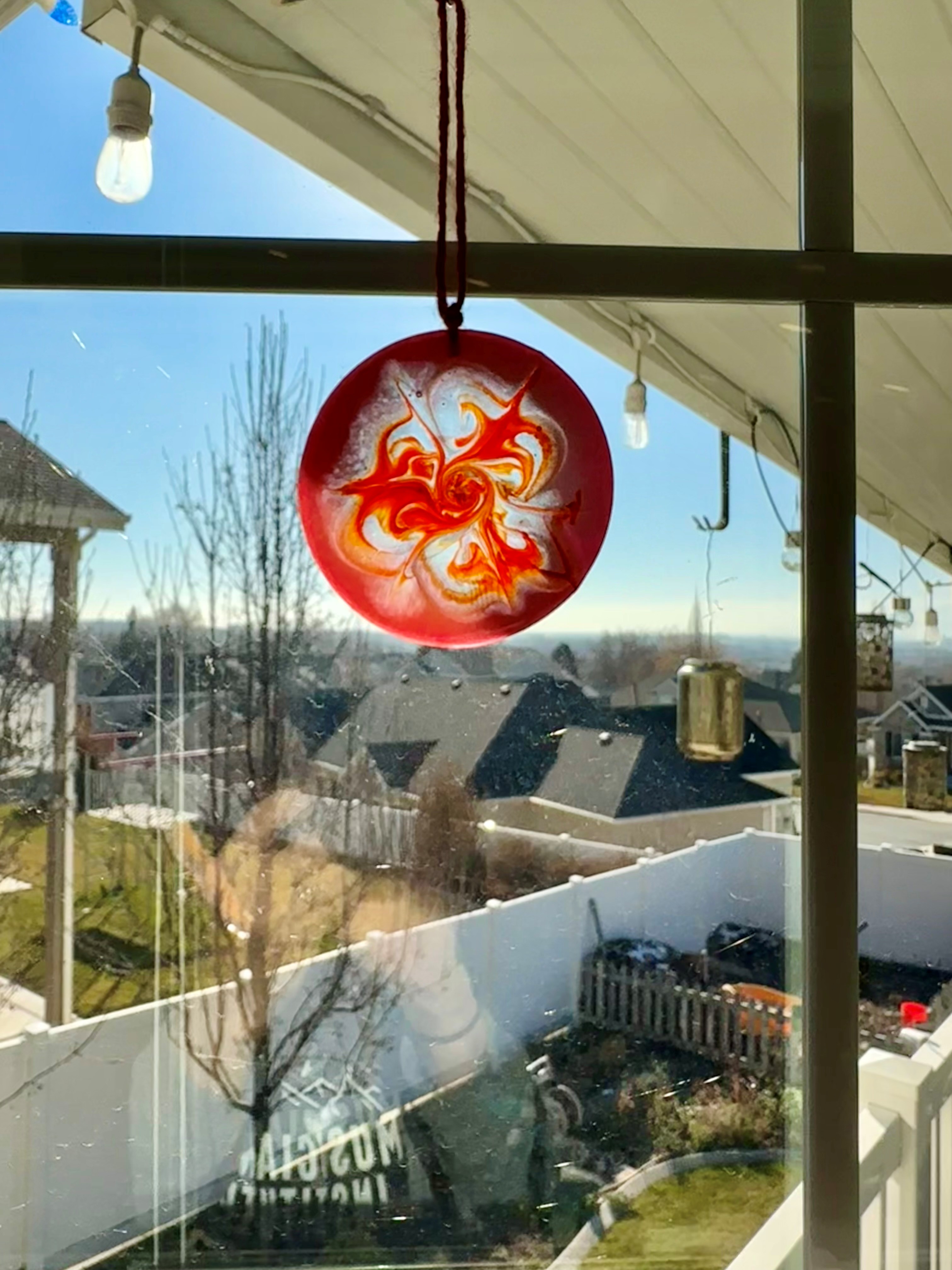 A luminous coaster-sized resin pour that hangs as a sun-catcher in a window with orange and red glowing effects